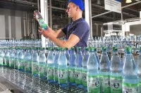 Eine Fachkraft für Lebensmitteltechnik prüft eine Mineralwasserflasche an einer Abfüllanlage in Bad Liebenwerda.