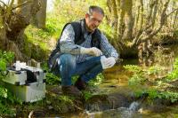 Eine Fachkraft für Wasserwirtschaft entnimmt Proben zur Überprüfung der Wasserqualität eines Flusses.
