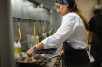 Eine Fachfrau für Systemgastronomie kocht ein deftiges Fleischgericht in einer Pfanne.