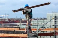 Ein Gerüstbauer transportiert Holzbretter für ein Gerüst auf einer Baustelle.