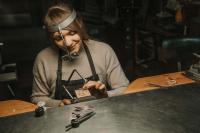 Eine Goldschmiedin arbeitet in ihrer Werkstatt an Schmuck.