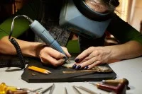 Eine Graveurin bringt ein Muster auf einem Metallstück an.