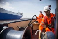 Zwei Hafenschiffer auf einem Schlepper holen ein Seil ein.