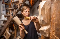 Eine Holzbildhauerin bearbeitet eine Skulptur mit Knüpfel und Beitel.