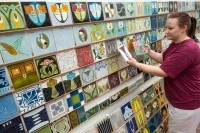 Eine Industriekeramikerin Verfahrenstechnik begutachtet eine Reihe von Jugendstilfliesen mit verschiedenen Motiven.