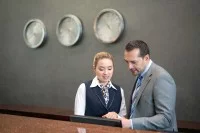 Ein Kaufmann für Hotelmanagement informiert sich bei seiner Kollegin am Empfang über die Reservierungen des Hotels, um den Personaleinsatz der nächsten Wochen besser planen zu können.