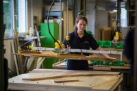 Eine Klavier- und Cembalobauerin hebt in der Werkstatt im C. Bechstein Centrum Sachsen ein Instrumententeil zur Montage auf ein Klavier.