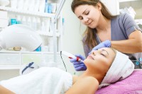 Eine Kosmetikerin behandelt das Gesicht ihrer Kundin mit einem Mesotherapiegerät.