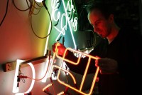 Ein Leuchtröhrenglasbläser prüft eine Neonreklame in der Neonmanufactur in Berlin.
