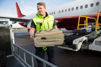 Ein Luftverkehrskaufmann hebt Gepäck von einem Flugzeug auf einen Gepäckwagen.