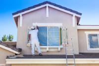 Ein Maler und Lackierer bemalt die Fensterläden und -rahmen an einem Haus mit weißer Farbe.