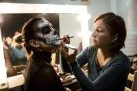 Eine Maskenbildnerin schminkt das Gesicht einer Frau mit einem Totenkopfmotiv.