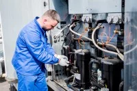 Ein Mechatroniker für Kältetechnik überprüft die Temperatursensoren im Kühlversorgungsbereich eines Lüftungsgerätes.