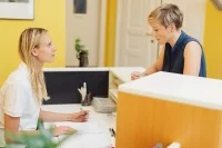 Eine Medizinische Fachangestellte spricht am Empfang einer Praxis mit einer Patientin.