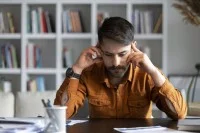 Ein Berufsschullehrer sitzt zuhause am Schreibtisch und stützt den Kopf auf die Hände.