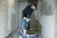 Eine Fachkraft für Holz-und Bautenschutzarbeiten rührt Sanierputz an.