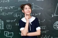 Eine nachdenkliche Schülerin steht vor einer schwarzen Tafel auf der mathematische Formeln angeschrieben sind.