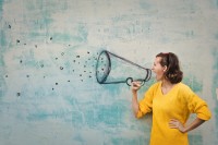 Eine Frau schreit durch ein Megafon, welches als Graffiti an die Wand gemalt ist. 