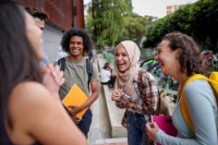 Fünf junge Menschen mit unterschiedlicher ethnischer Herkunft stehen im Kreis und lachen. Sie halten Schulsachen in den Händen.