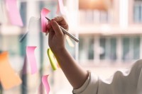 Eine weibliche Hand schreibt auf ein Post-it an einer Workshop-Wand