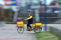 Eine Fachkraft für Kurier-, Express- und Postdienstleistungen der Deutschen Post fährt mit ihrem Dienstfahrrad durch ein Wohngebiet in Schwerin.