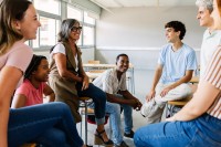 Ein Klassenraum,  in dem eine Lehrerin mit sechs Lernenden im lockeren Stuhlkreis sitzt.