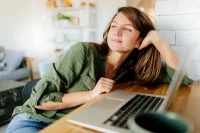 Junge Frau denkt am Laptop nach