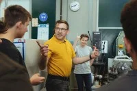 Ein Lehrer und drei Auszubildende stehen vor Maschinen und diskutieren.