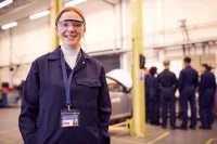 Junge Frau mit anderen Auszubildenden in einer Autowerkstatt