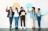 Fünf junge, fröhliche Menschen lehnen an einer Wand halten Sprechblasen aus Papier hoch.