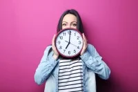 Eine Frau hält eine große runde Uhr vor sich.