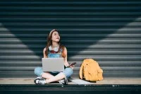 junge Frau im Schneidersitz mit Laptop und Smartphone
