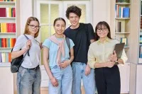 Zwei Schülerinnen, ein Schüler und eine Lehrerin stehen in der Bibliothek und lächeln in die Kamera.