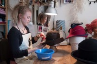 Eine Modistin bügelt eine Hutkrempe in einem Atelier.