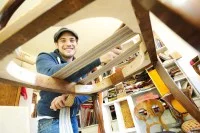 Ein Polsterer bestückt einen alten Stuhl mit einem neuen Polster.