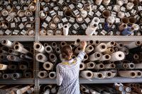 Eine Produktgestalterin - Textil wählt Stoff aus einem Stapel von Rollen in einer Textilwerkstatt aus.