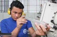 Eine Produktionsfachkraft Chemie der Firma Hermes Schleifmittel kontrolliert ein Werkstück aus Metall.