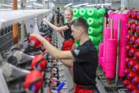 Zwei Mitarbeiter einer Spulerei für Textilveredlung wechseln Spulen mit farbigem Garn. 