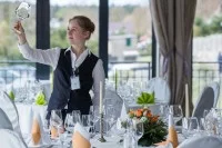 Eine Restaurantfachfrau kontrolliert an einem eingedeckten Tisch die Gläser.