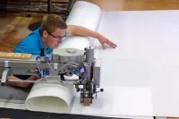 Ein Segelmacher näht mit einer speziellen, im Fußboden eingelassenen Nähmaschine verschiedene Teile eines Segels zusammen.