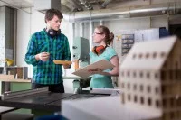 Eine Technische Modellbauerin bespricht mit ihrem Kollegen den Bau eines dreidimensionalen Gebäudemodells.