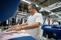 Ein Textilreiniger bügelt Kleidung mit einer Dampfbügelmaschine.