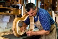 Ein Zupfinstrumentenmacher schleift die Seitenwand eines Gitarrenkorpus.