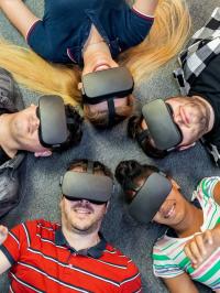 Berufsschülerinnen und Berufsschüler liegen mit VR-Brille im Kreis auf dem Boden.