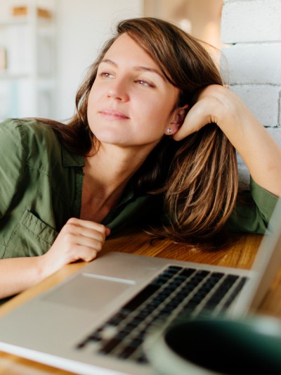 Junge Frau denkt am Laptop nach