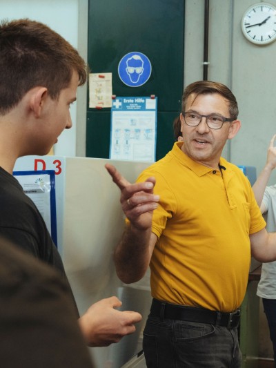 Ein Lehrer und drei Auszubildende stehen vor Maschinen und diskutieren.