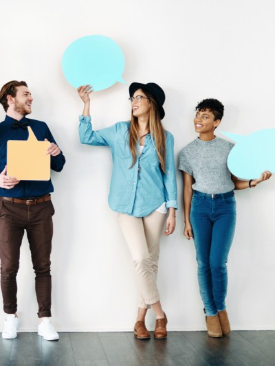 Fünf junge, fröhliche Menschen lehnen an einer Wand halten Sprechblasen aus Papier hoch.
