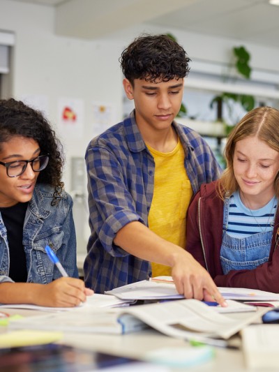 Fünf Schülerinnen und Schüler arbeiten zusammen an einem Tisch mit Heften und Büchern.