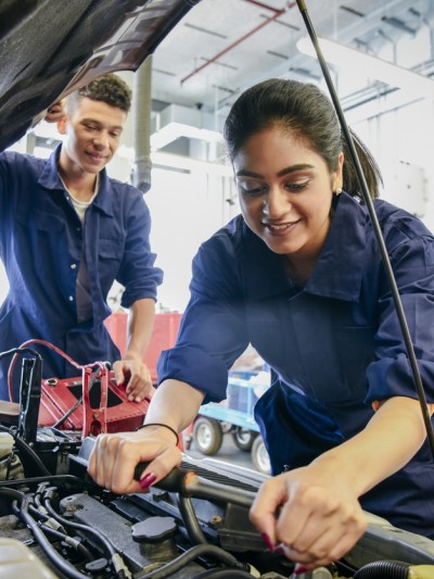 Auszubildende für Kraftfahrzeugmechatronik bei der Arbeit am Auto in der Werkstatt