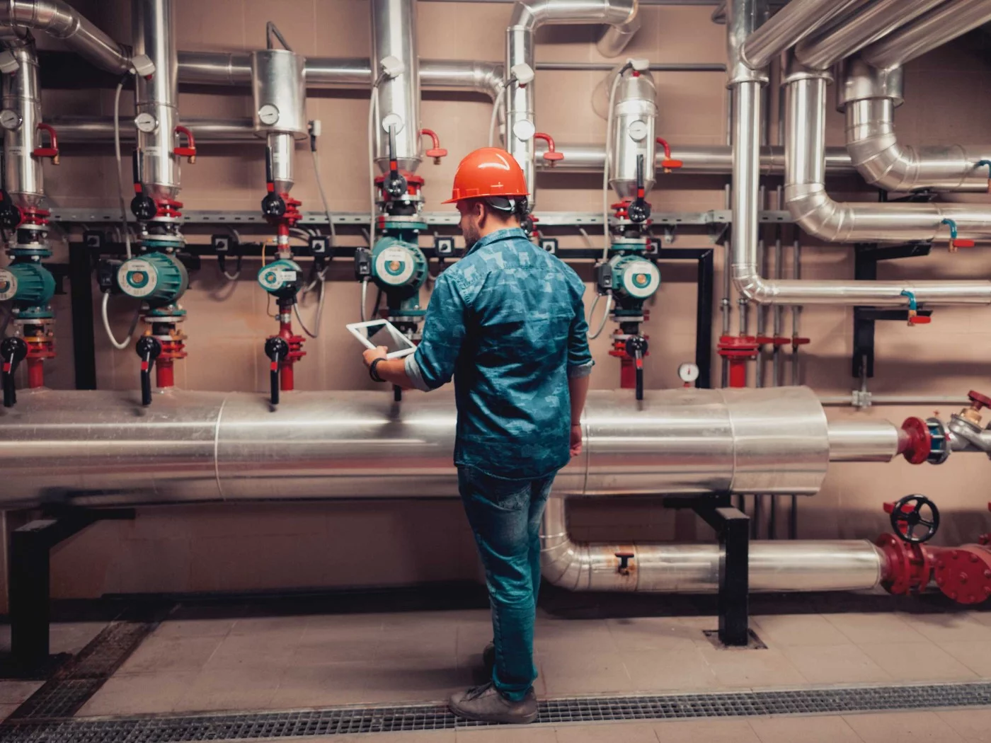 Ein Anlagenmechaniker überprüft Rohrleitungen und dokumentiert seine Ergebnisse auf einem Tablet.